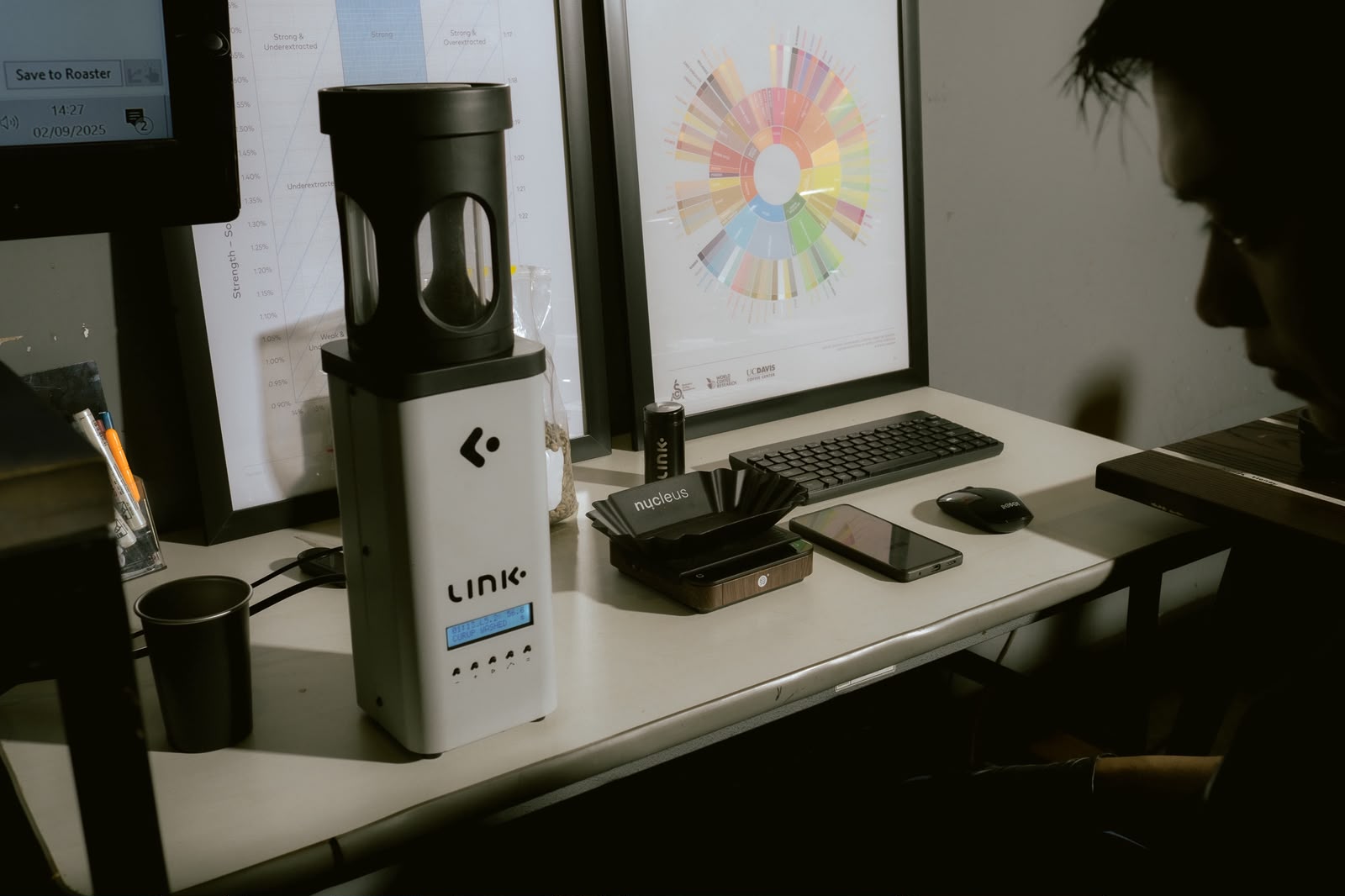 LINK moisture and density analyzer on the QA desk, with the SCA flavor wheel and an extraction chart behind
